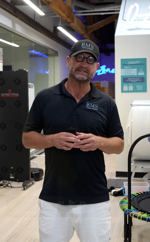 BMS Wellness founder in branded polo and hat inside the biohacking facility with red-light therapy panels