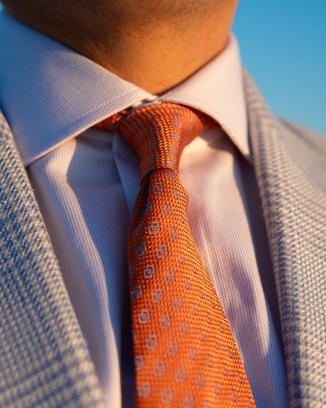 Franco Uomo close-up: orange knit tie against a blue houndstooth jacket at golden hour